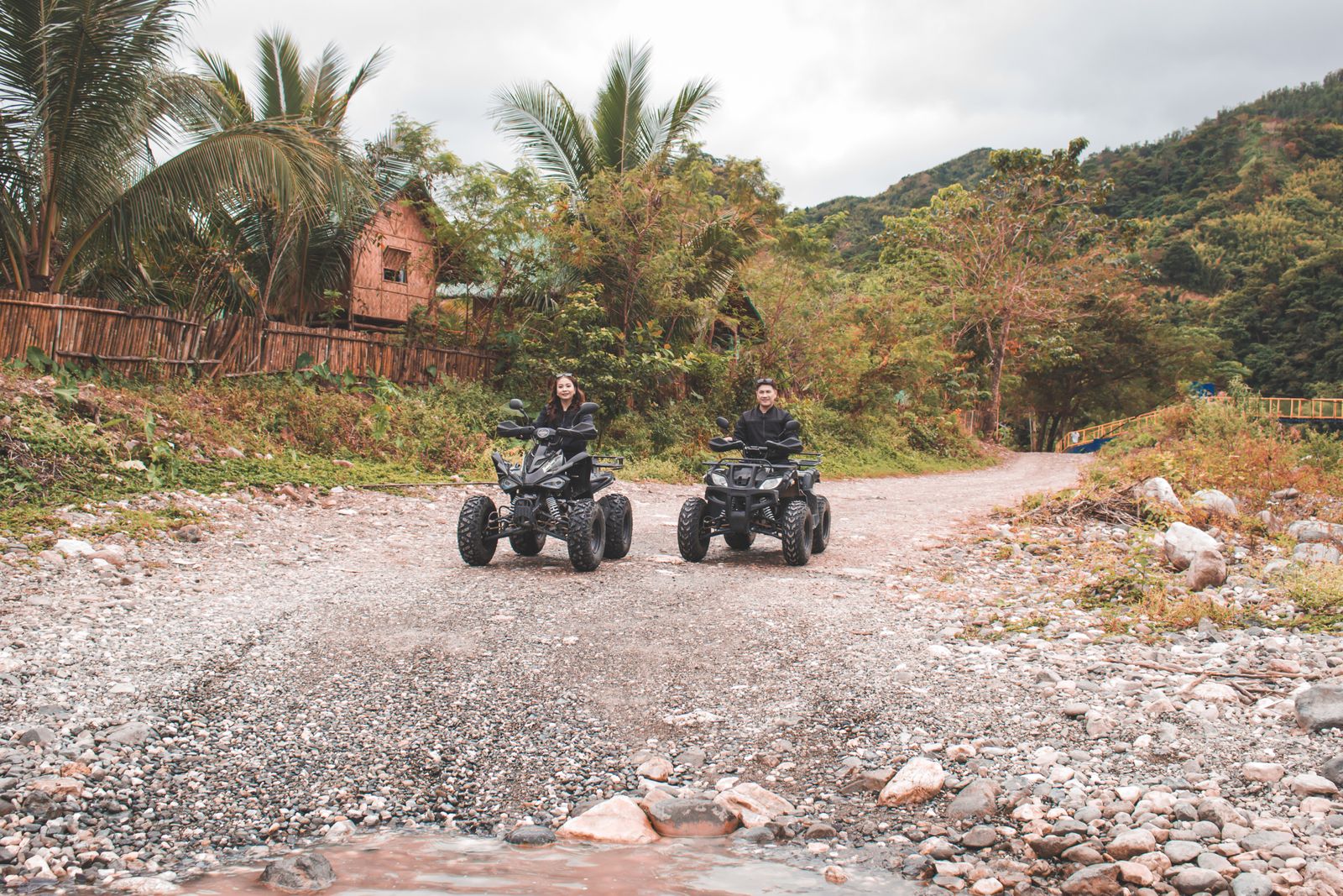 Two riders on four-wheelers cruising a palm-lined trail